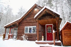 Una baita di legno con una porta rossa, circondata da alberi ricoperti di neve.