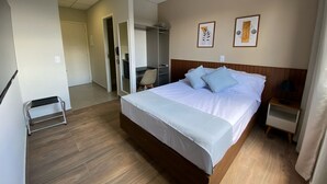 A hotel room with a large bed, a desk, and a chair. There is a wardrobe and a small table with a lamp. - NOBRE HOTEL (Cotia)