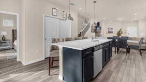 A modern kitchen with a central island, pendant lighting, and a staircase leading to an upper level.