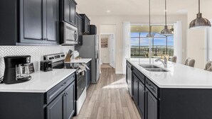 A modern kitchen with dark cabinetry, a large island with a sink, and pendant lighting.