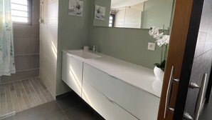 Une salle de bain moderne avec un grand miroir, un meuble-lavabo blanc et un espace douche.
