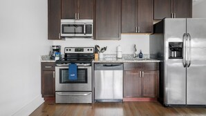 A modern kitchen with dark wood cabinets, stainless steel appliances including a microwave, oven, dishwasher, and refrigerator. - The Heart of Historic King St | Cooper Suite (Charleston)