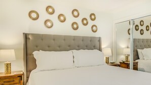 A neatly arranged hotel room with a tufted headboard, a large bed, two bedside tables with lamps, and a wall-mounted mirror. - 10 A, One Bedroom Condo (Miramar Beach)