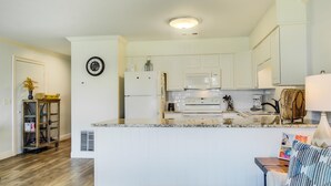 A modern kitchen with white cabinets, a central island, and a microwave. - 10 A, One Bedroom Condo (Miramar Beach)
