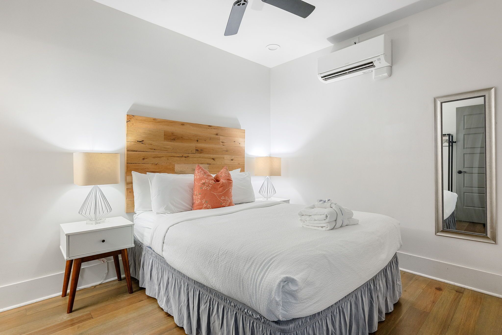 Une chambre à coucher bien rangée, avec une tête de lit en bois, du linge de lit blanc et une table de chevet sur laquelle se trouve une lampe.