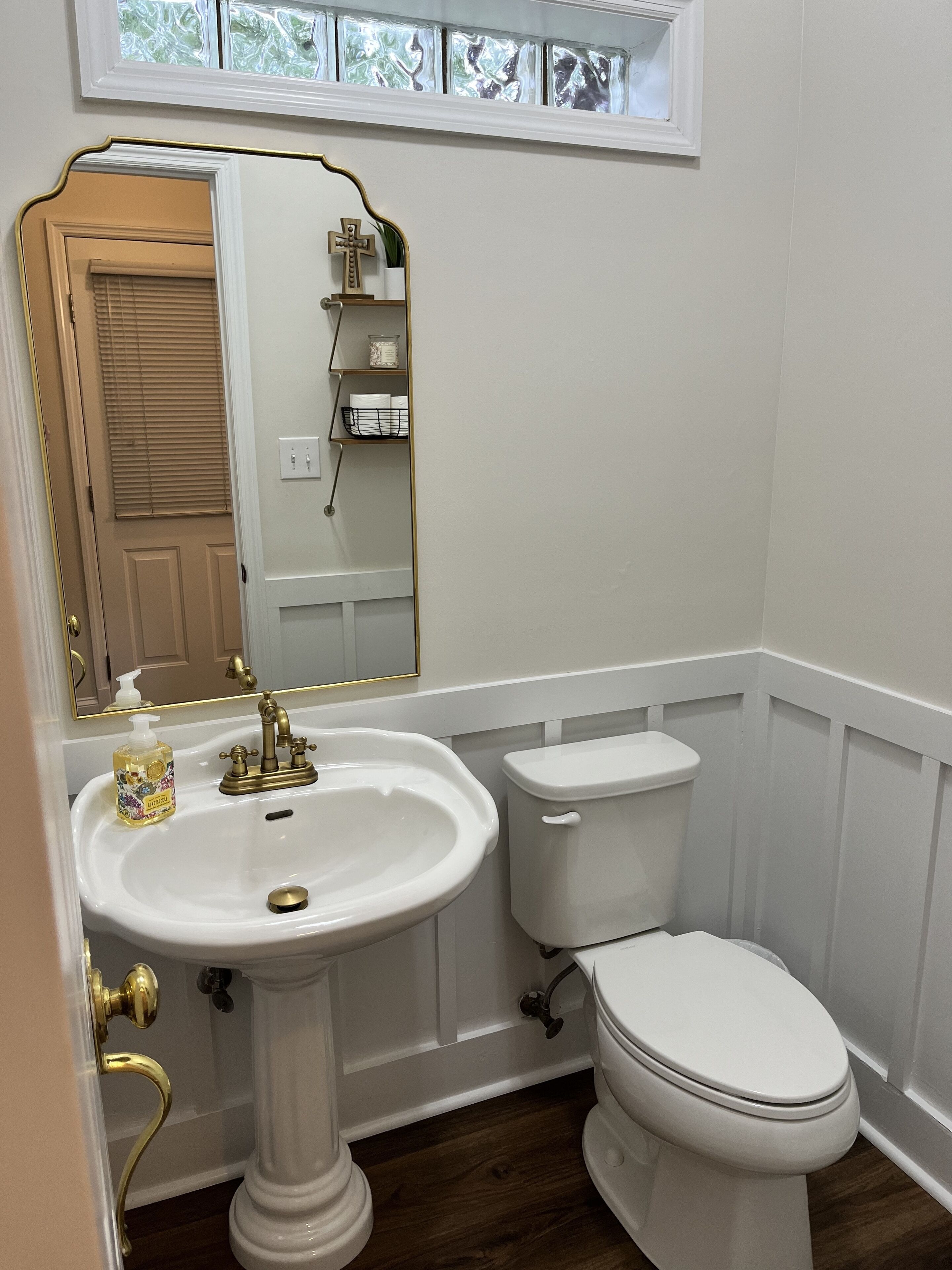 A bathroom with a pedestal sink, a toilet, and a window above the sink.