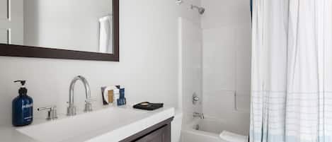Un baño con lavamanos blanco, espejo, inodoro y ducha con cortina.