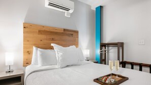 Hotelkamer met houten hoofdbord, bed met wit beddengoed, nachtkastje met lamp en dienblad met desserts en glazen op het bed.