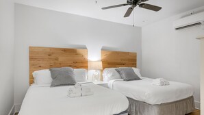 A hotel room with two beds, a wooden headboard, a ceiling fan, and an air conditioning unit. - In the Heart of King Street | Hampton Suite (Charleston)