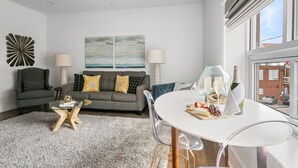 A modern living room with a grey sofa, a glass coffee table, and a dining table set for a meal. - In the Heart of King Street | Hampton Suite (Charleston)