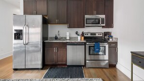 A modern kitchen with stainless steel appliances, dark wooden cabinets, and a granite countertop. - In the Heart of King Street | Hampton Suite (Charleston)