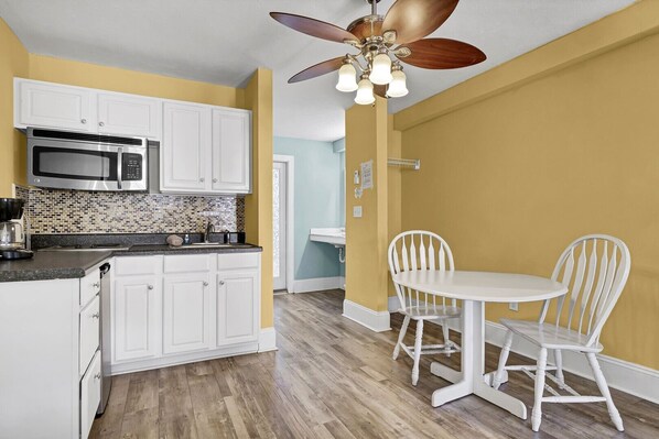 Enjoy meals in this kitchen with a microwave, tiled backsplash, and wooden flooring, adjacent to a dining area with a table and chairs.