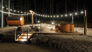 A wooden cabin with a hot tub, outdoor seating, and string lights in a forest setting. - C_AL RANCH WELLNESS CORTINA, LAKE CADORE, DOLOMITES (PIEVE DI CADORE)