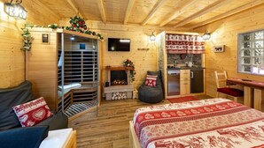 A cozy wooden cabin room with a bed, a sofa, a fireplace, a television, and a small kitchen area. - C_AL RANCH WELLNESS CORTINA, LAKE CADORE, DOLOMITES (PIEVE DI CADORE)
