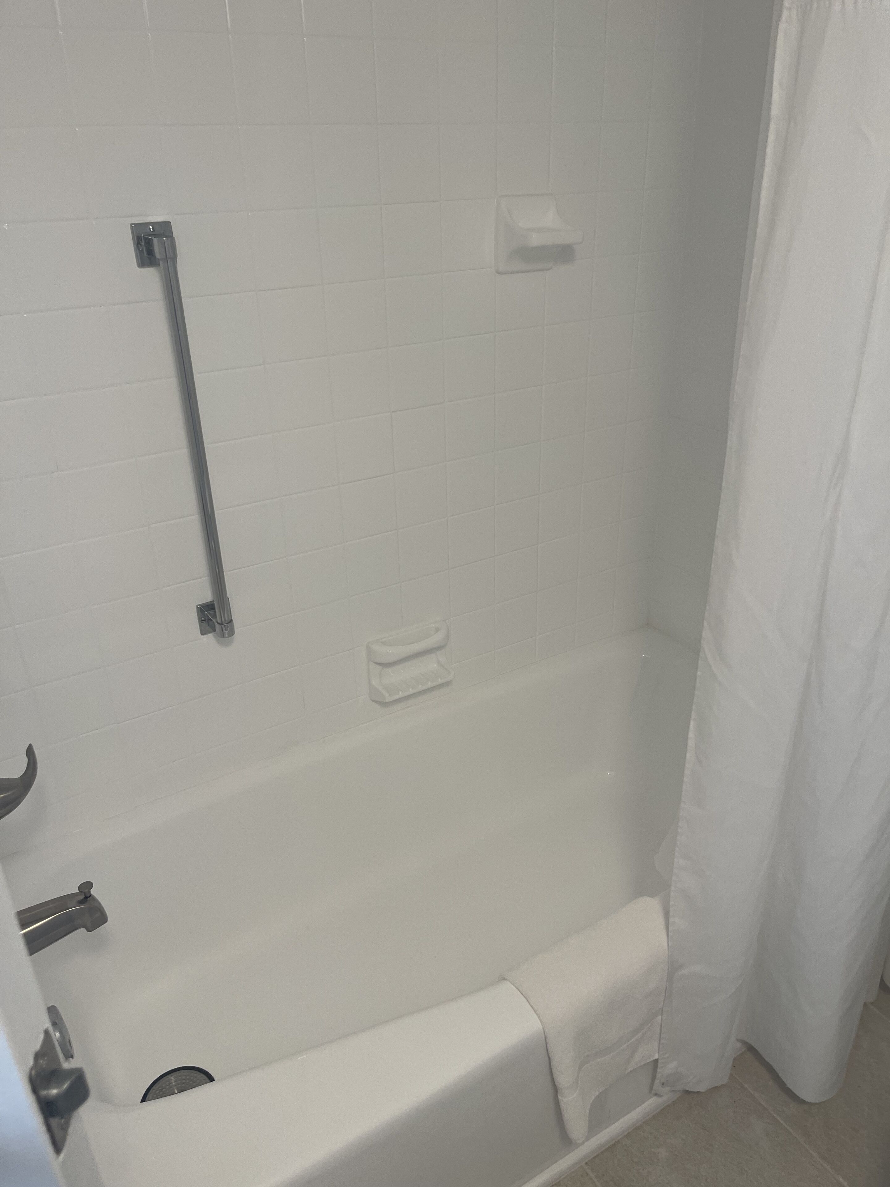 Une salle de bain avec une baignoire blanche, une barre d’appui et un rideau de douche.