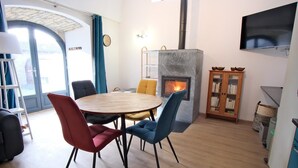 A modern living room with a round wooden table, colorful chairs, a fireplace, a bookshelf, and a TV mounted on the wall.