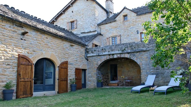A stone building with a courtyard, featuring two wooden doors, an arched entrance, and a seating area with chairs and a table.