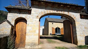 A stone archway leading to a building with wooden doors and a tiled roof.