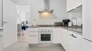 Una cocina moderna con armarios blancos, horno empotrado, microondas y cafetera.