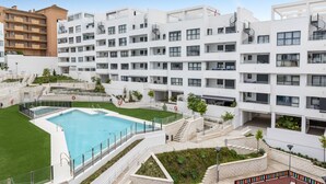 Un moderno edificio de apartamentos con piscina central, varios balcones y un jardín bien cuidado.
