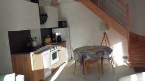 A compact kitchen with modern appliances, a dining area with a table and chairs, and a wooden staircase. - Maison à 50 m de la mer (Saint-Jacut-de-la-Mer)