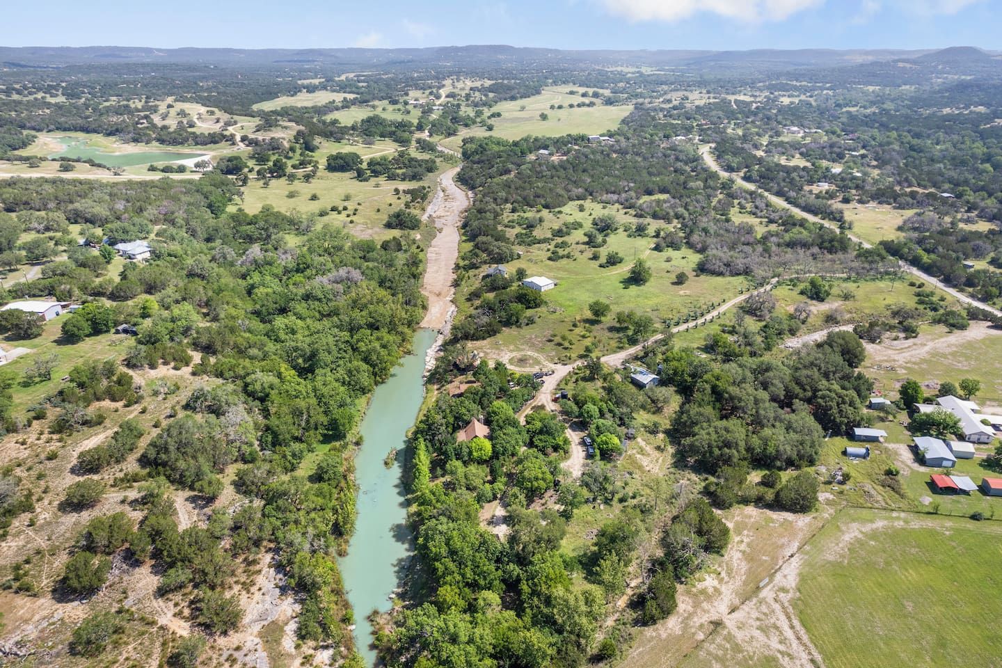 A rural landscape with a river, scattered buildings, and green fields.