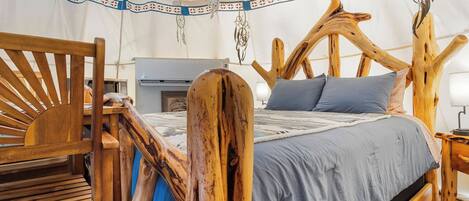 A tent with a bed featuring a wooden headboard, a bench, and a hanging dreamcatcher.