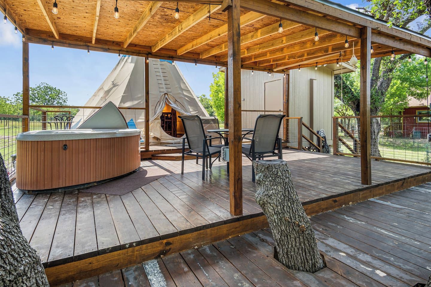 A wooden deck with a hot tub, chairs, and a tent structure.