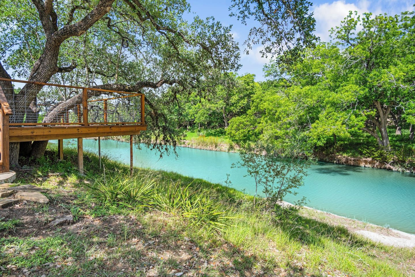 Une terrasse en bois surplombant une rivière aux eaux d’un bleu limpide, entourée d’une végétation luxuriante.