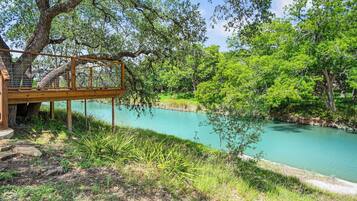 Une terrasse en bois surplombant une rivière aux eaux d’un bleu limpide, entourée d’une végétation luxuriante.