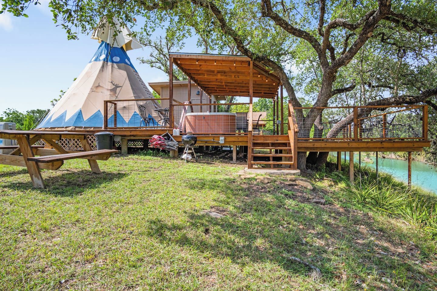 Une terrasse en bois dotée d’un espace salon couvert, d’une table de pique-nique et d’une structure en forme de tipi.