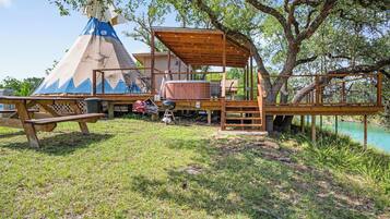 Une terrasse en bois dotée d’un espace salon couvert, d’une table de pique-nique et d’une structure en forme de tipi.
