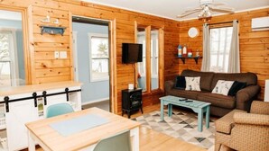 A cozy cabin-style room with a wooden interior, a dining table, a sofa, and a television. - Escape to Tranquility at The Sandy Pearl: A Cozy Log Cottage Retreat (Tatamagouche)