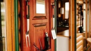 A wooden cabin with a red door, a small window, and a coat hanging on the door. - Escape to Tranquility at The Sandy Pearl: A Cozy Log Cottage Retreat (Tatamagouche)