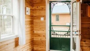 A wooden cabin room with a bed, a window, and a door leading outside. - Escape to Tranquility at The Sandy Pearl: A Cozy Log Cottage Retreat (Tatamagouche)