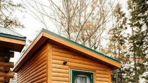 A log cabin with a green door and a wooden porch. - Escape to Tranquility at The Sandy Pearl: A Cozy Log Cottage Retreat (Tatamagouche)
