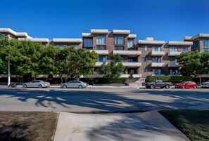 Un moderno edificio residencial de varios pisos, con diseño de techo plano, ventanas grandes y un jardín frontal ajardinado.