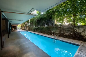 Una piscina con un borde de hormigón, rodeada por un muro de piedra y abundante vegetación.