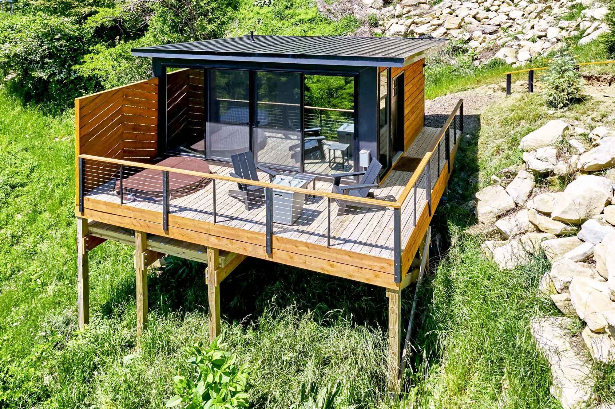 A wooden deck with a glass enclosure, outdoor furniture, and a stone wall in the background.