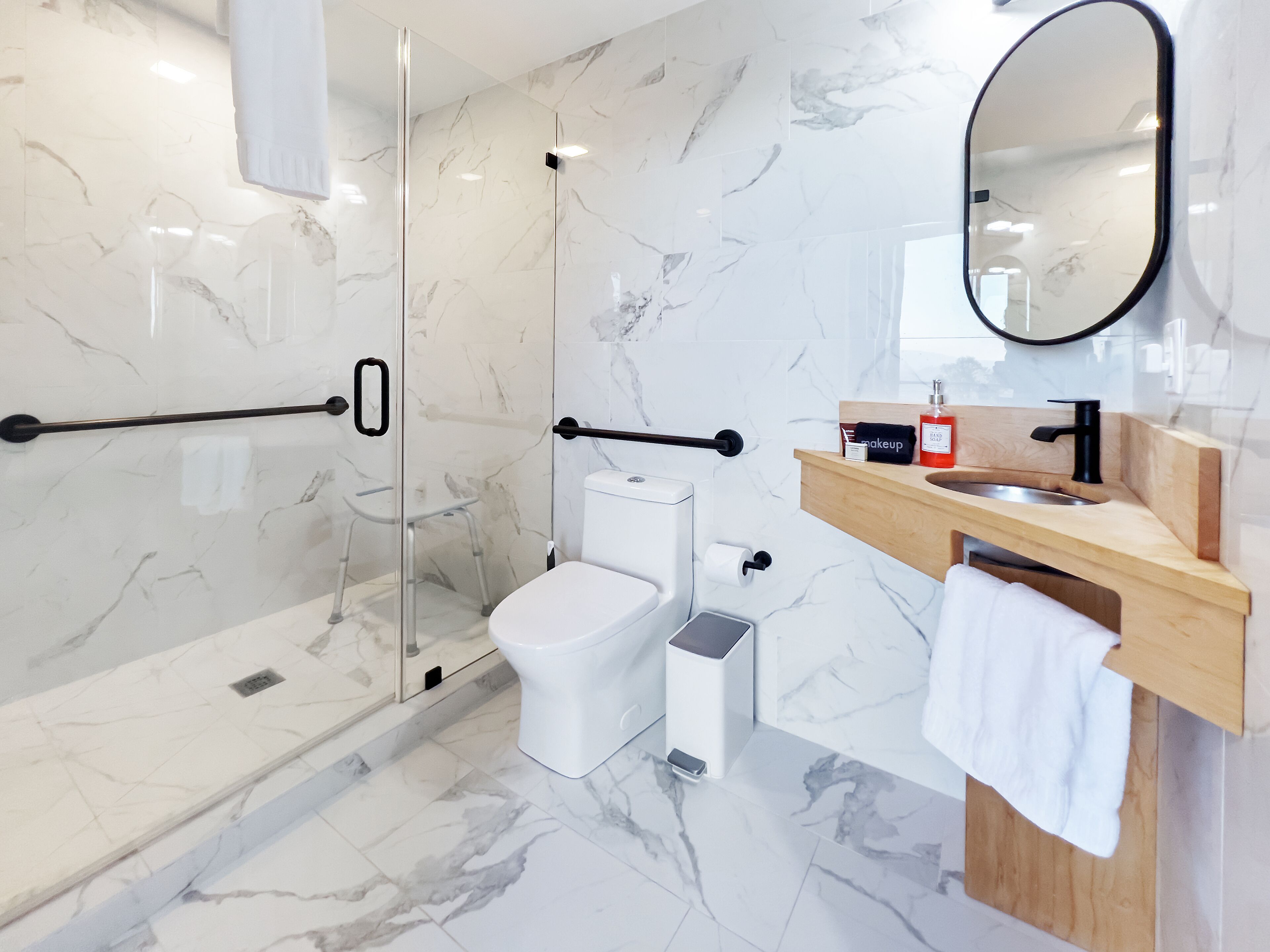 A modern bathroom with a glass shower enclosure, a white toilet, a sink with a wooden countertop, and a mirror above the sink.