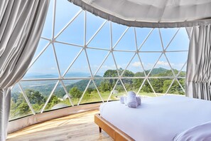 Ein Zimmer mit großem Fenster, einem Bett und Blick auf eine grüne Landschaft.