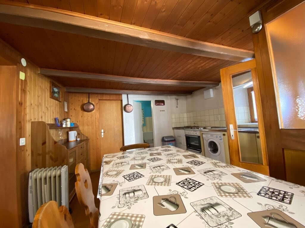 A compact kitchen with wooden walls, a radiator, a table with a patterned tablecloth, and a washing machine.