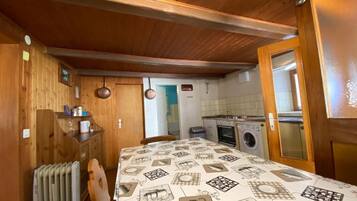 A compact kitchen with wooden walls, a radiator, a table with a patterned tablecloth, and a washing machine.