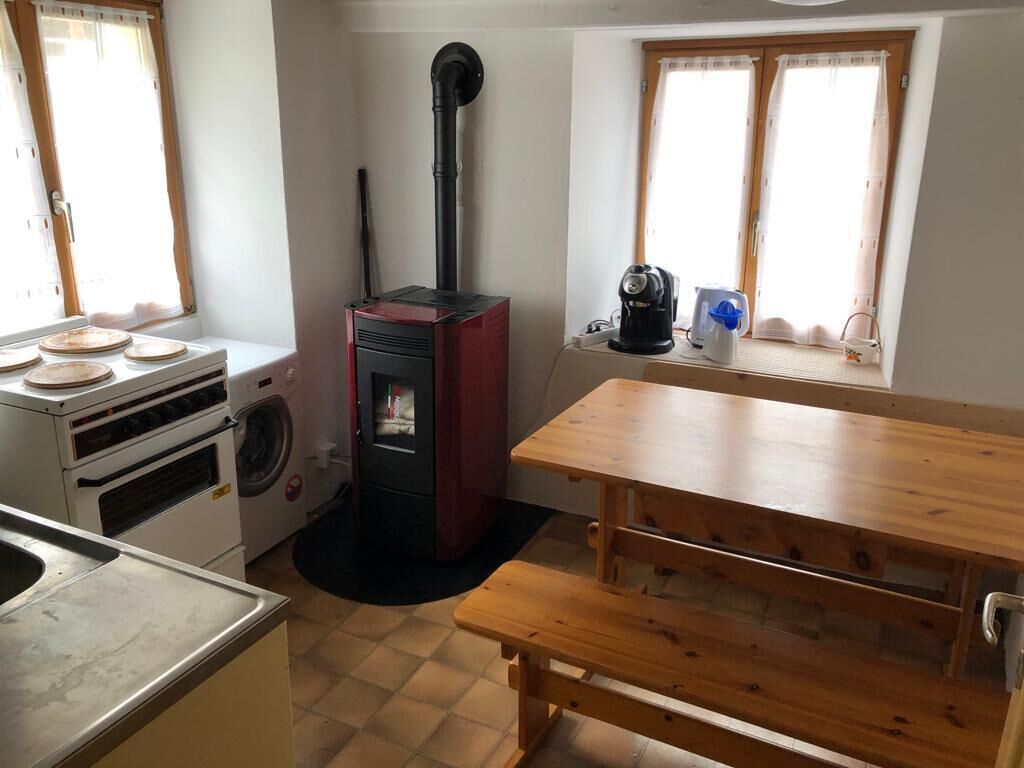 A compact kitchen with a wood-burning stove, a washing machine, and a dining table with benches.