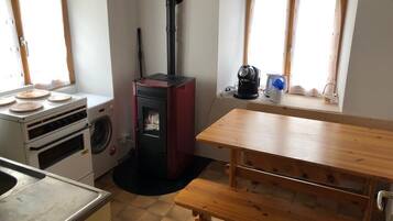 A compact kitchen with a wood-burning stove, a washing machine, and a dining table with benches.