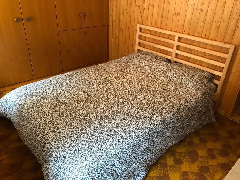 Ein Schlafzimmer mit einem Holzkopfteil, einem Bett mit einem gemusterten Bettüberwurf und einem Holzschrank.