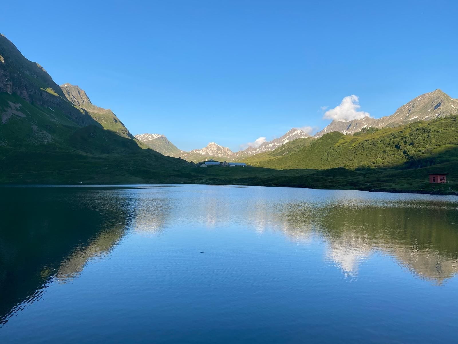 Un lac paisible, avec des montagnes en arrière-plan et un petit bâtiment sur la droite.