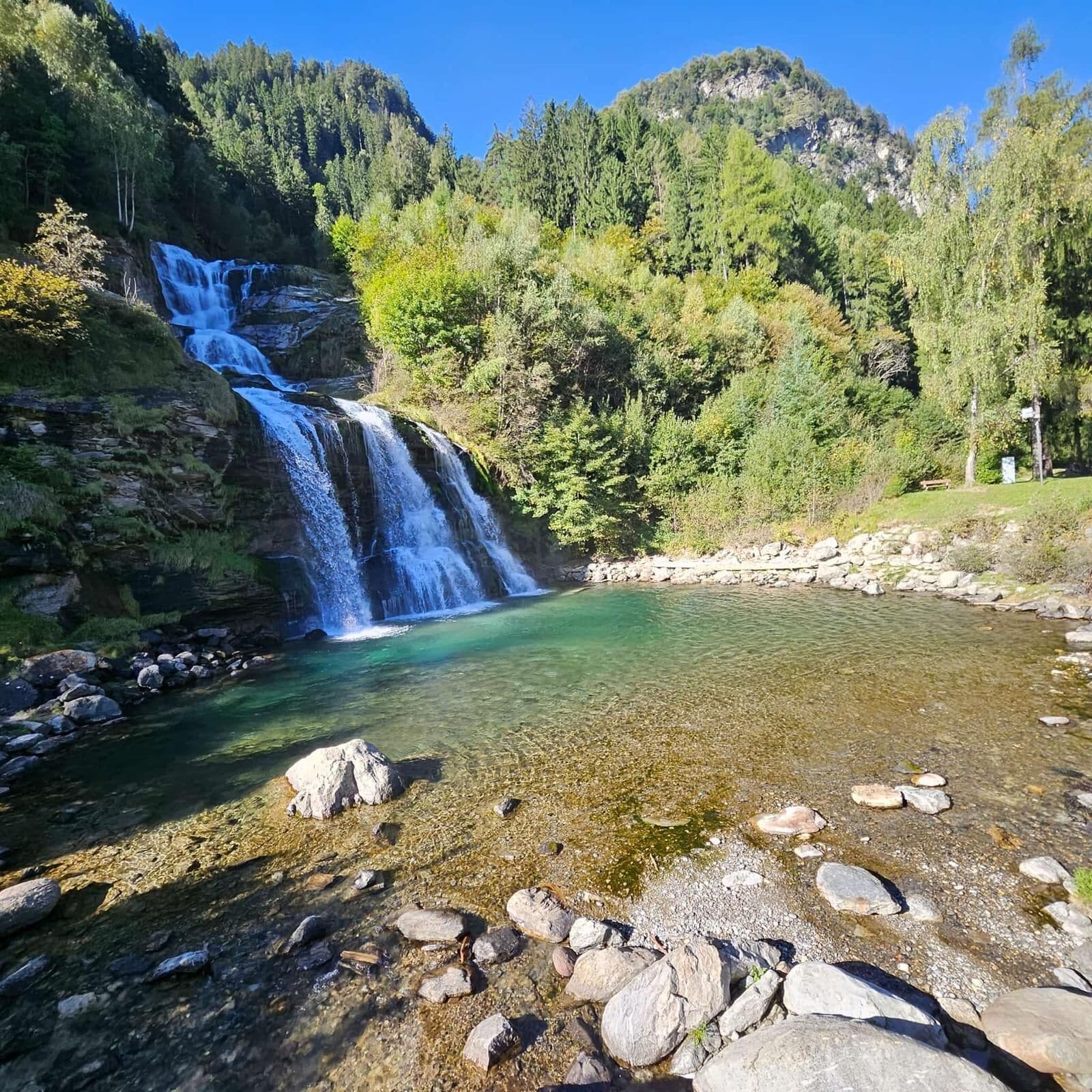 A waterfall cascading into a clear river surrounded by forested hills.