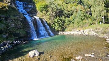 A waterfall cascading into a clear river surrounded by forested hills.