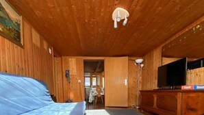A room with wooden walls and ceiling, a grey carpet, two blue-covered sofas, a wooden cabinet with a television, and a painting on the wall. - Chalet del Sole  (Quinto)